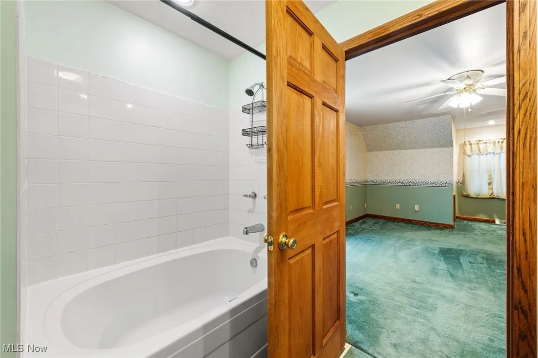Bathroom featuring wallpapered walls, carpet floors, bathtub / shower combination, and a ceiling fan