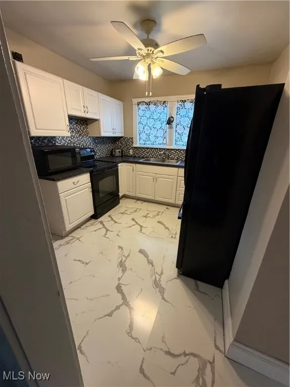 Kitchen featuring tasteful backsplash, refrigerator, light marble finish flooring, range, and white cabinetry