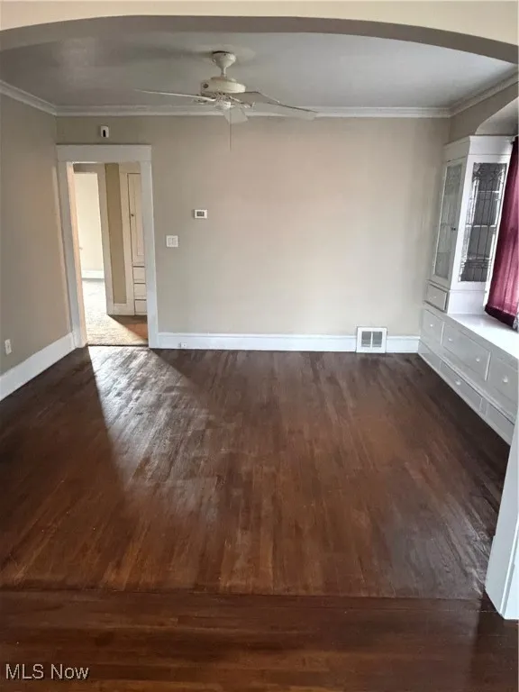 Empty room with arched walkways, ornamental molding, dark wood finished floors, and a ceiling fan