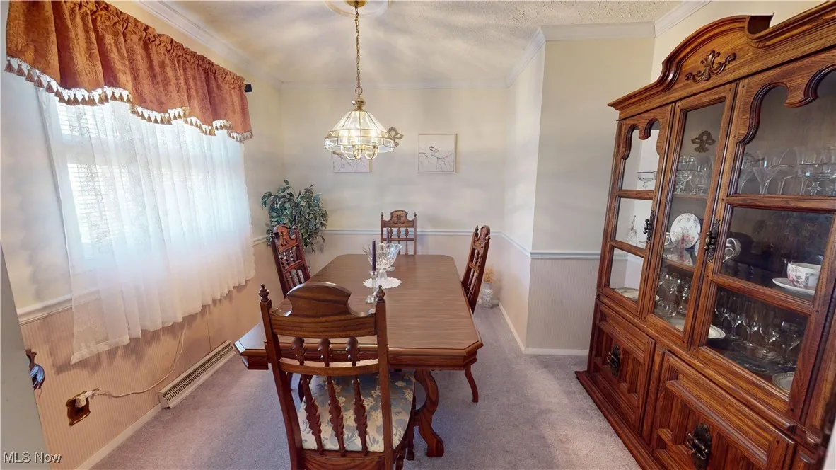 Dining room featuring carpet flooring, a baseboard radiator, ornamental molding, and a chandelier