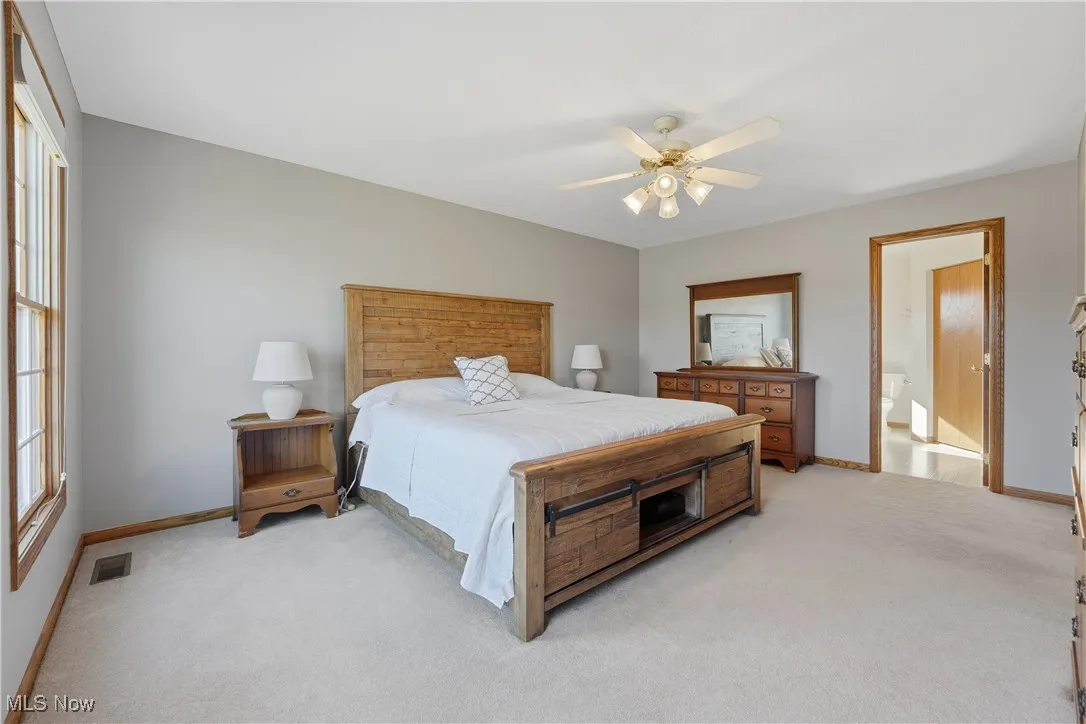 Bedroom featuring light colored carpet, a ceiling fan, and connected bathroom