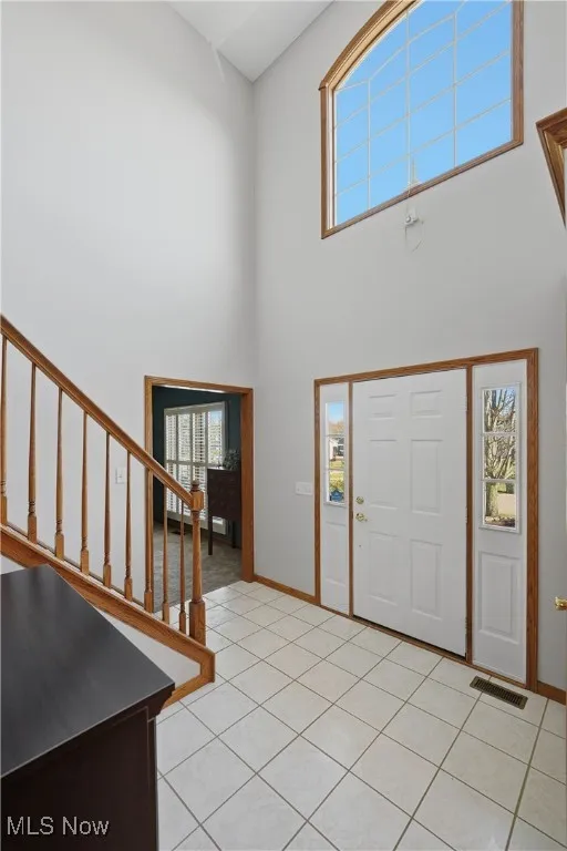 Foyer entrance featuring healthy amount of natural light, light tile patterned floors, stairway, and a towering ceiling