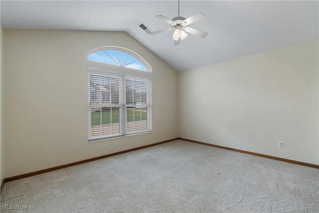 Light-filled secondary bedroom featuring a vaulted ceiling, arched transom window, and ceiling fan—neutral palette makes it an easy guest room, office, or hobby space.