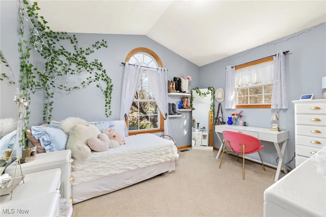 Bedroom with vaulted ceiling, light colored carpet, and multiple windows