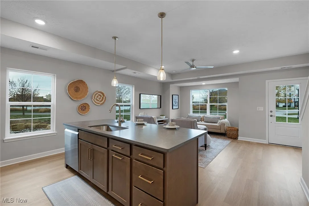 Kitchen featuring an island with sink, open floor plan, dark brown cabinets, ceiling fan, and healthy amount of natural light