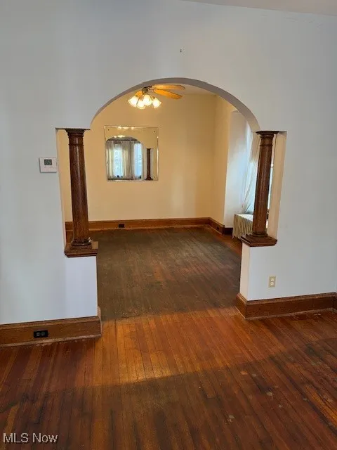 Room featuring dark wood-type flooring, arched walkways, ceiling fan, and ornate columns