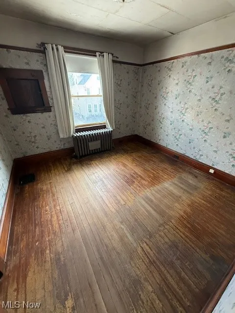 Room featuring wallpapered walls, wood-type flooring, and radiator