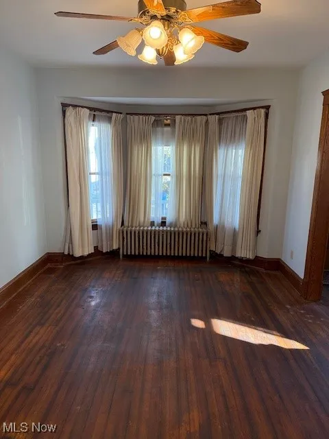 Room with ceiling fan, dark wood-style flooring, and radiator