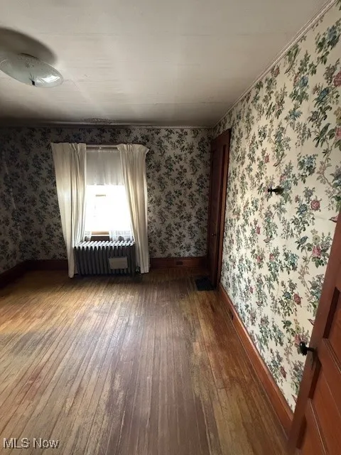 Room with wood-type flooring and wallpapered walls