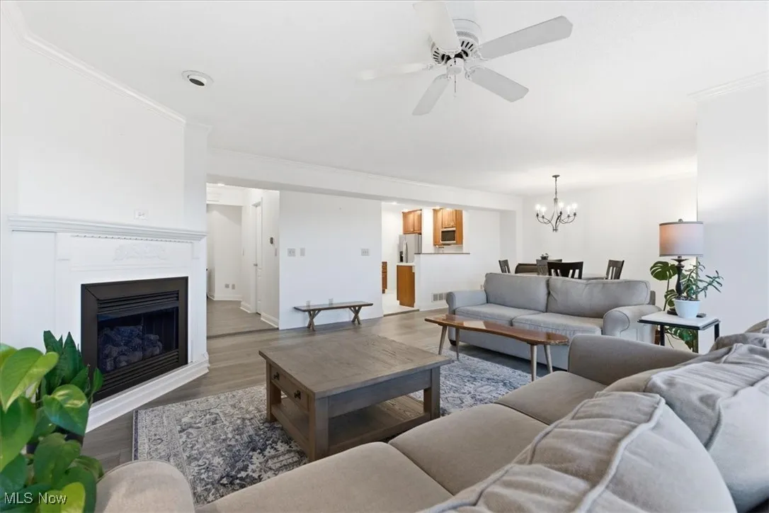 Living area with wood finished floors, ornamental molding, a fireplace, a ceiling fan, and a chandelier