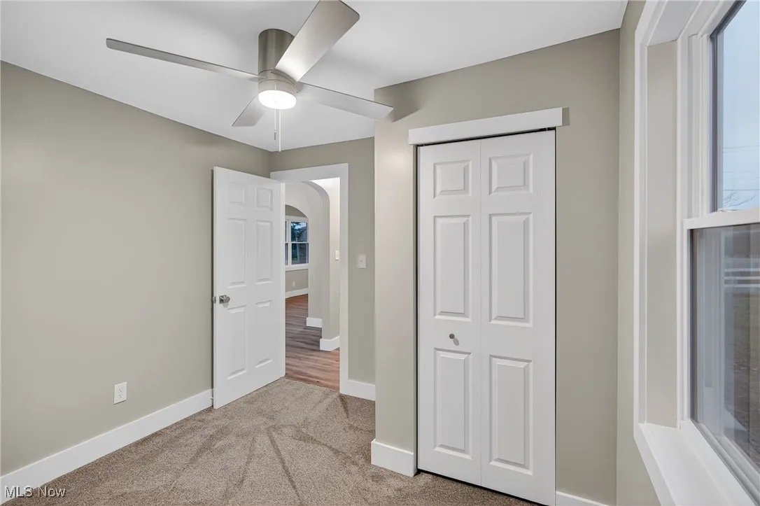 Unfurnished bedroom featuring light colored carpet, arched walkways, a closet, and ceiling fan