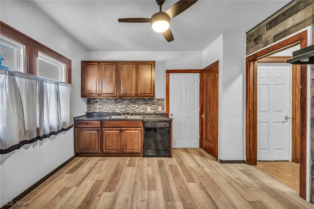Kitchen with black dishwasher, dark countertops, brown cabinets, backsplash, and light wood-style flooring