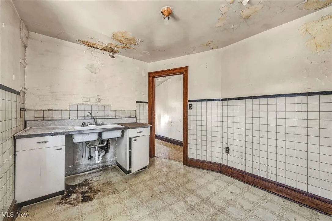 Kitchen featuring light flooring, tile walls, white cabinetry, and a wainscoted wall
