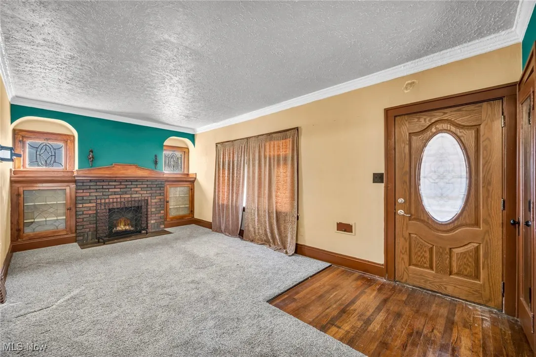 Foyer entrance featuring crown molding, a textured ceiling, a brick fireplace, dark carpet, and dark wood finished floors