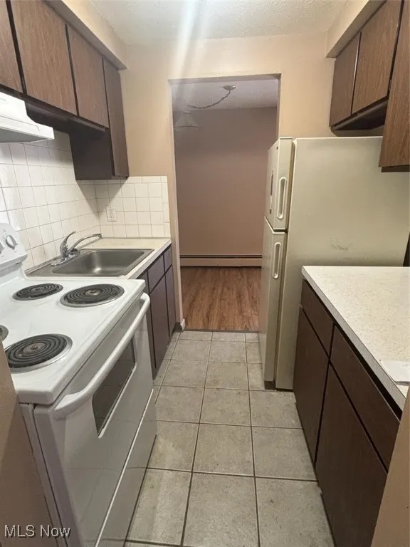 Kitchen with dark brown cabinetry, range, light countertops, and a textured ceiling