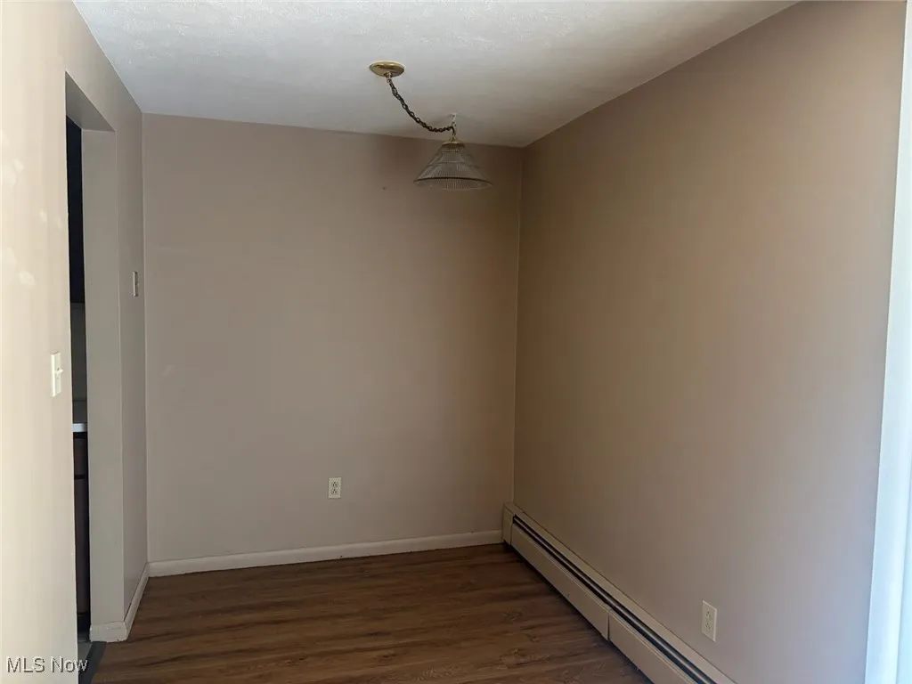 Spare room featuring a baseboard radiator and dark wood finished floors