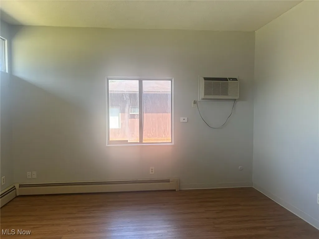 Unfurnished room featuring dark wood-type flooring, a baseboard radiator, and a wall mounted air conditioner