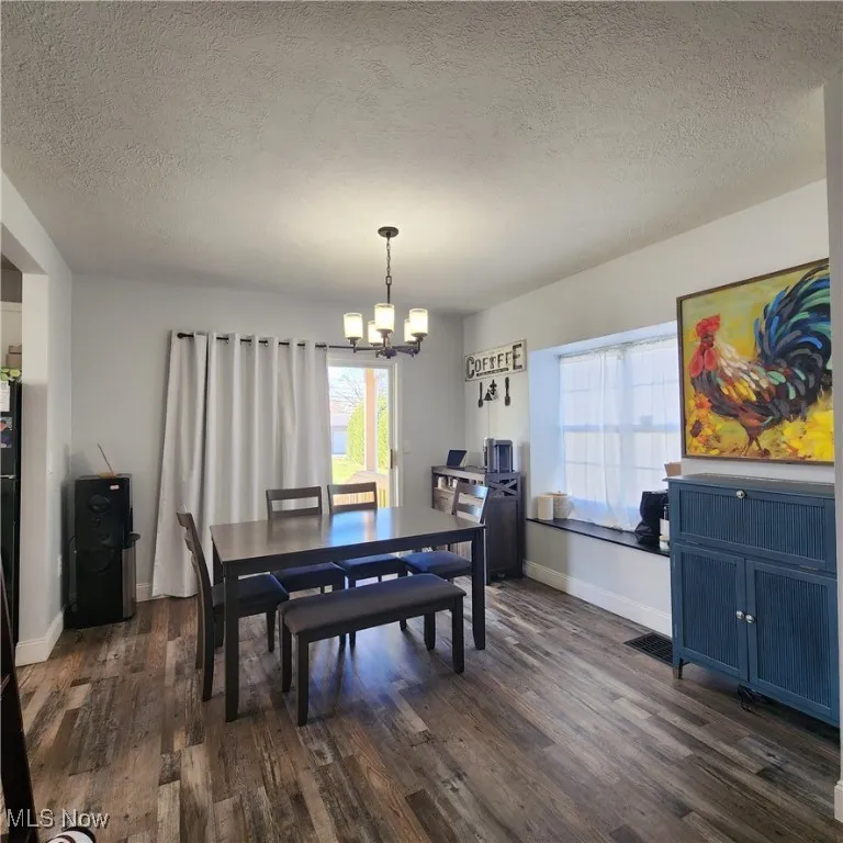 Dining room featuring a textured ceiling, healthy amount of natural light, dark wood-style flooring, and a chandelier