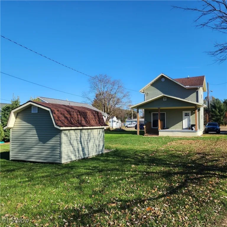Back of house featuring a storage shed, a porch, a yard, and a gambrel roof