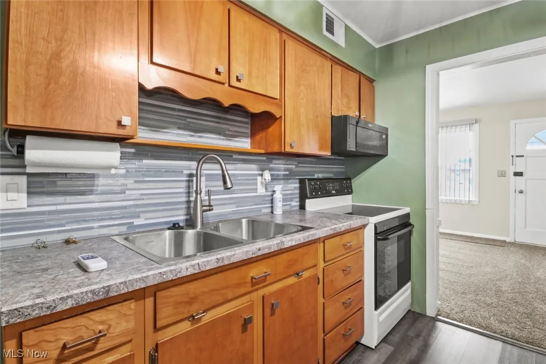 Kitchen featuring tasteful backsplash, white electric range, brown cabinets, black microwave, and light countertops