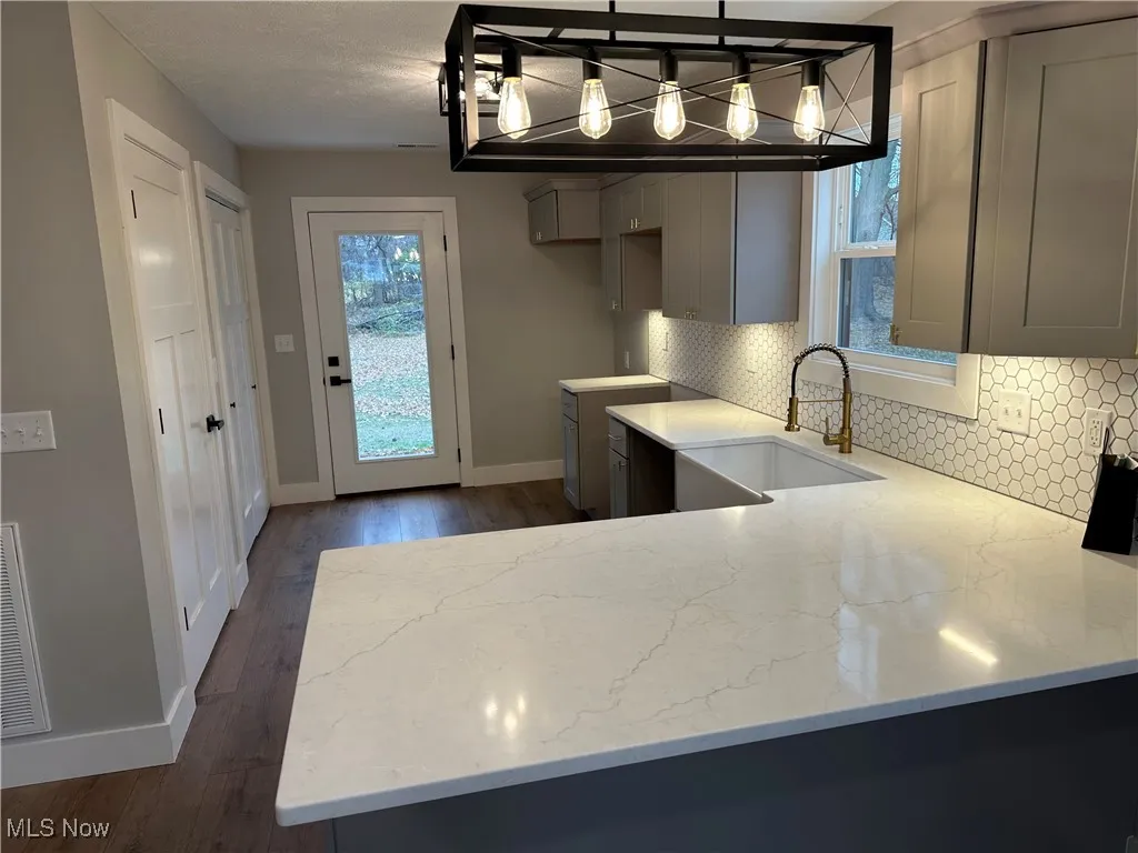 Kitchen featuring gray cabinetry, tasteful backsplash, dark wood-LVT floors, and light stone counters