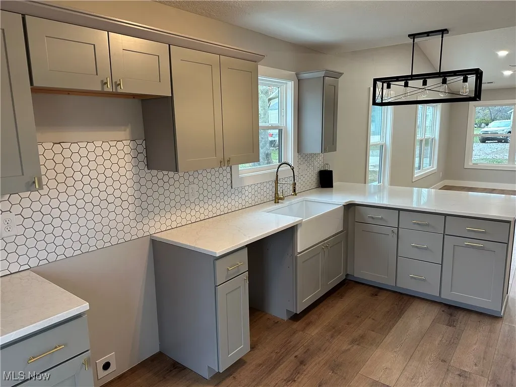 Kitchen with gray cabinetry, decorative backsplash, light stone counters, dark wood finished floors, and decorative light fixtures