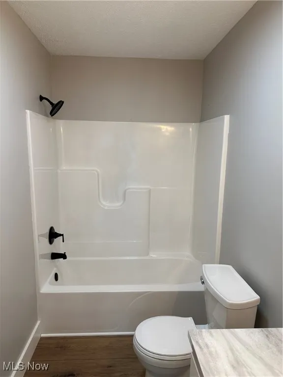 Full bathroom featuring LVT dark wood-look flooring, vanity, a textured ceiling, and washtub / shower combination