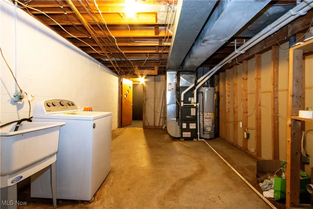 Unfinished basement featuring washer / clothes dryer, heating unit, and water heater