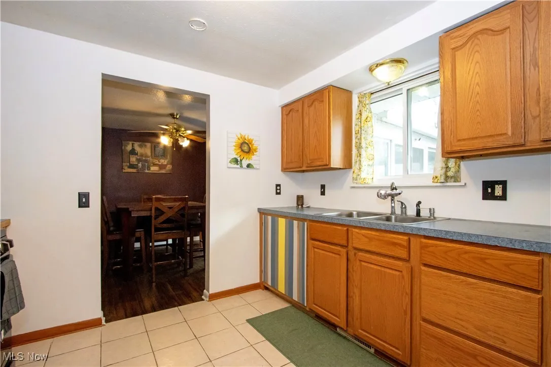 Kitchen with light tile patterned flooring, dark countertops, brown cabinetry, and ceiling fan