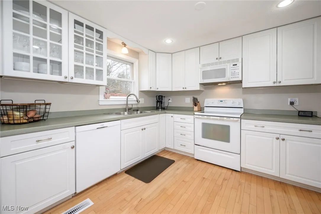 Kitchen featuring white appliances, white cabinetry, wood floors, land recessed lighting