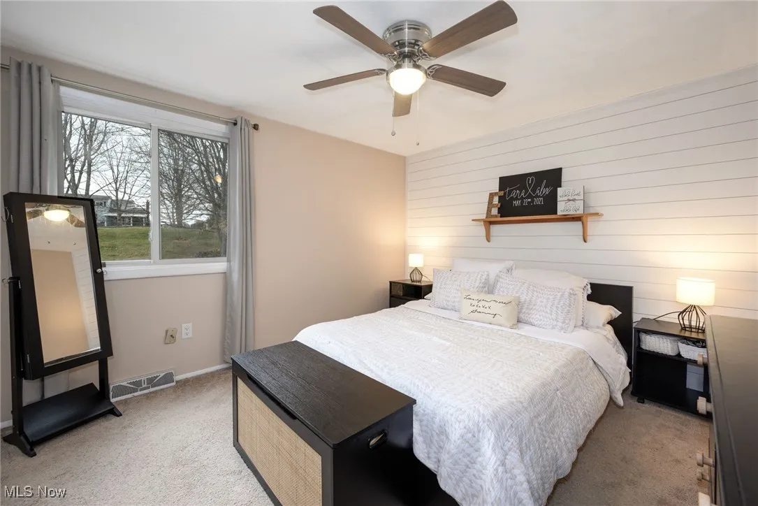 Bedroom featuring light colored carpet, shiplap wall decor and a ceiling fan