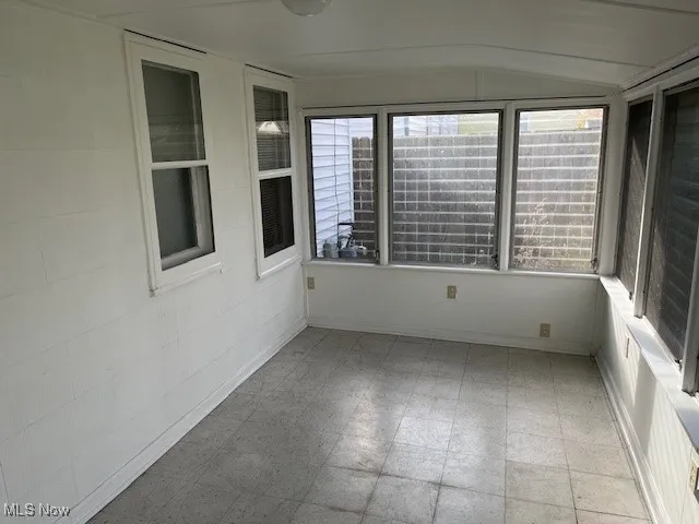 Unfurnished sunroom featuring tile patterned floors and vaulted ceiling