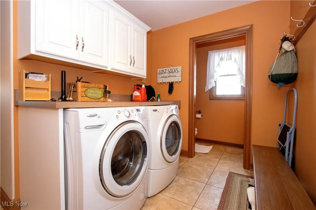 Laundry room with separate washer and dryer, light tile patterned floors, and cabinet space