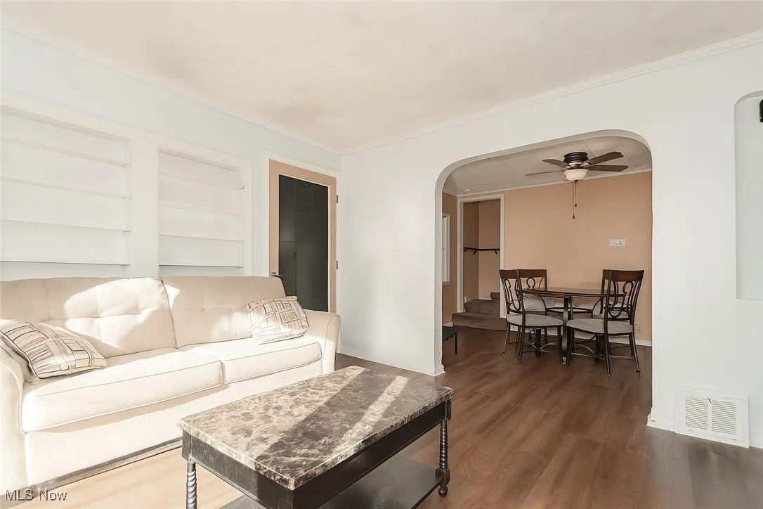 Living area featuring arched walkways, wood finished floors, ceiling fan, crown molding, and built in shelves