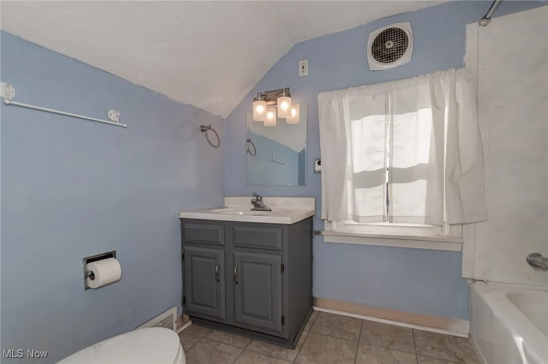 Full bathroom featuring lofted ceiling, vanity, light tile patterned floors, and tub / shower combination