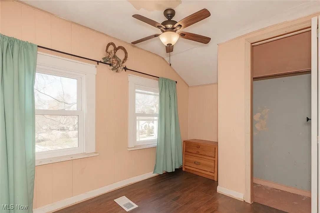 Unfurnished bedroom with dark wood-style flooring, lofted ceiling, and a ceiling fan