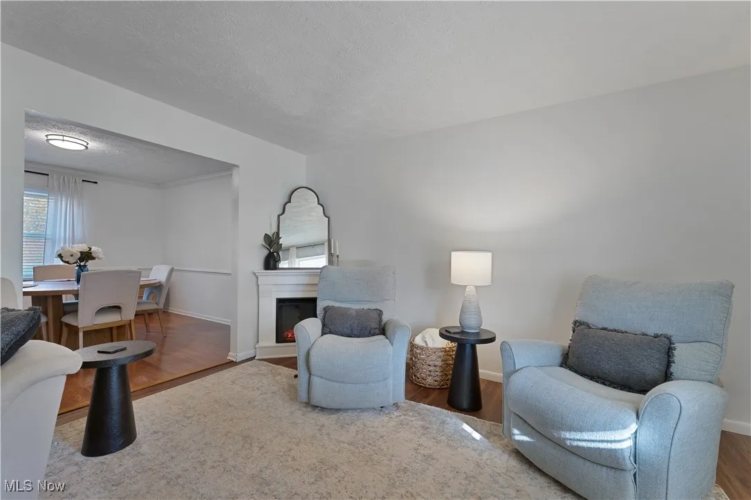 Living area with a textured ceiling, wood finished floors, and a lit fireplace