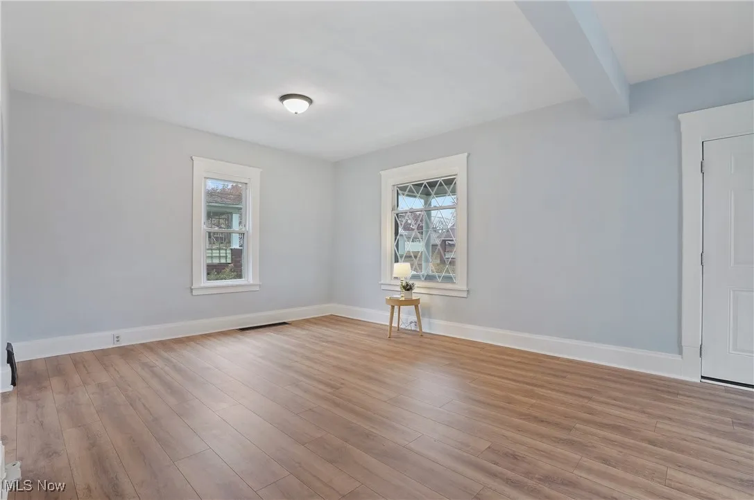 Unfurnished room featuring healthy amount of natural light, light wood-type flooring, and beam ceiling