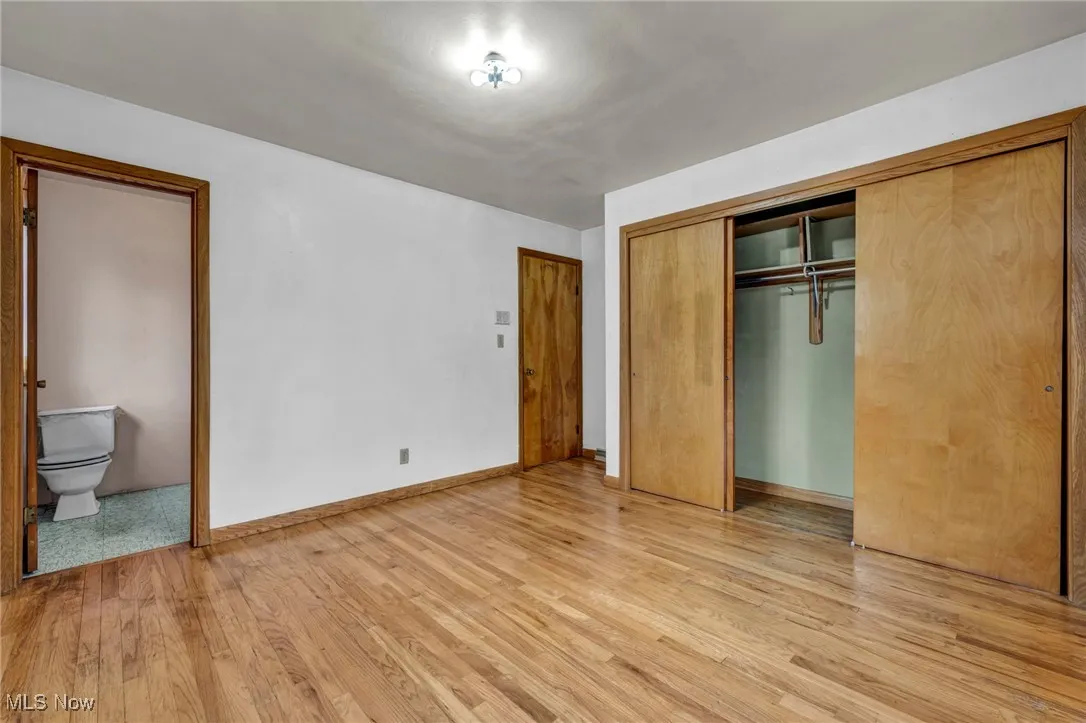 Unfurnished bedroom with ensuite bathroom, light wood-style floors, and a closet