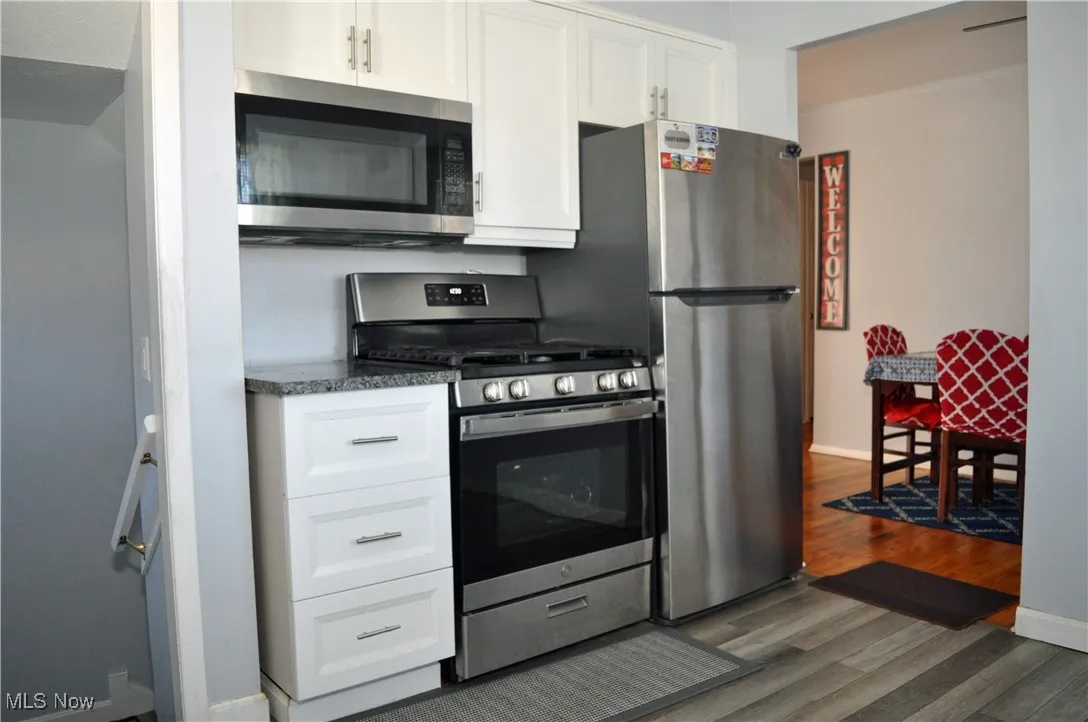 Kitchen with stainless steel appliances, white cabinetry, dark wood finished floors, and dark countertops