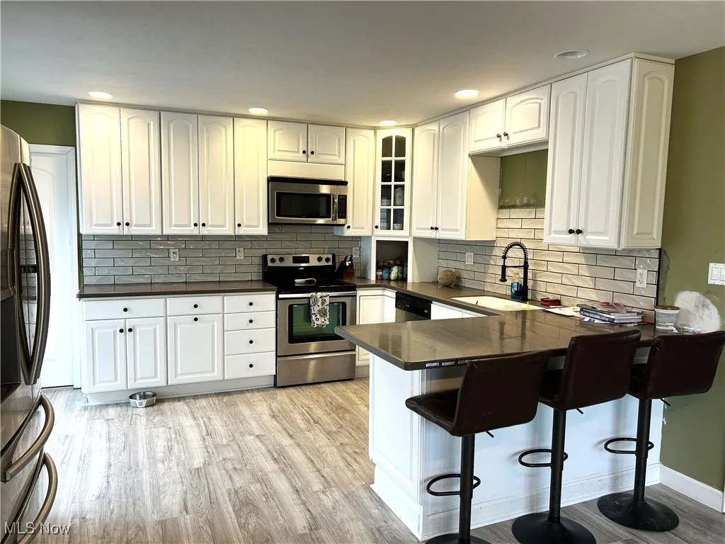 Kitchen featuring stainless steel appliances, white cabinetry, glass insert cabinets, a peninsula, and a kitchen bar