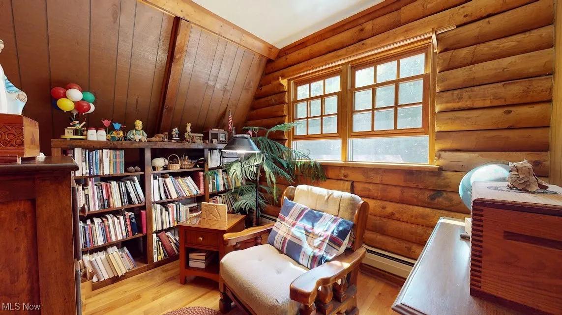 Sitting room featuring light wood-type flooring, baseboard heating, rustic walls, and vaulted ceiling
