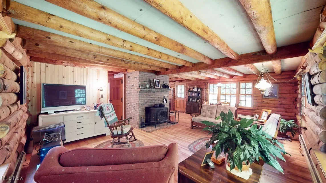 Living room featuring a wood stove, beam ceiling, wood finished floors, rustic walls, and baseboard heating