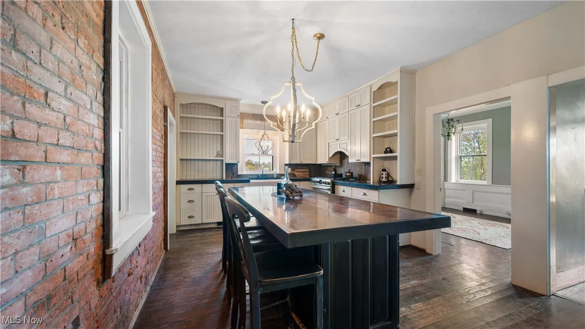 Kitchen featuring open shelves, dark wood finished floors, dark countertops, pendant lighting, and brick wall