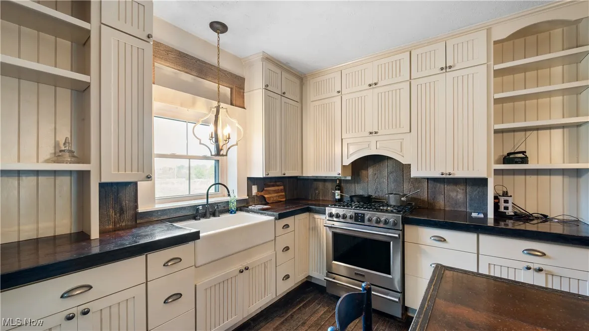 Kitchen featuring cream cabinetry, open shelves, stainless steel range with gas cooktop, and pendant lighting