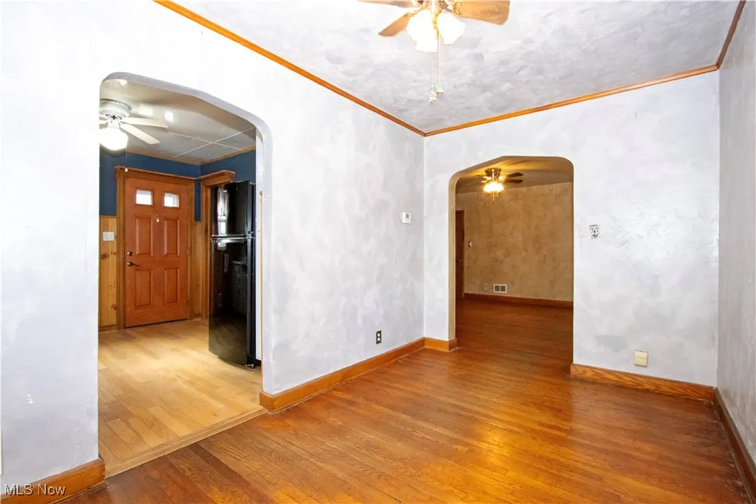 Unfurnished room with ceiling fan, light wood-type flooring, arched walkways, and ornamental molding