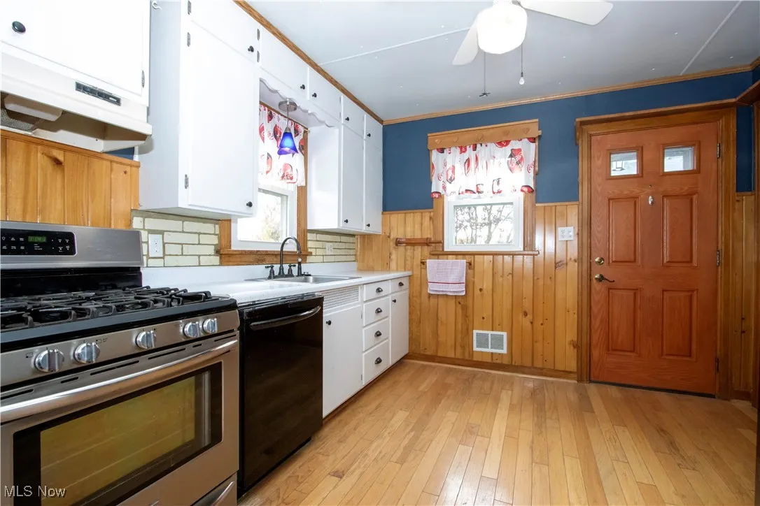 Kitchen featuring gas range, wood walls, white cabinets, light wood-type flooring, and light countertops