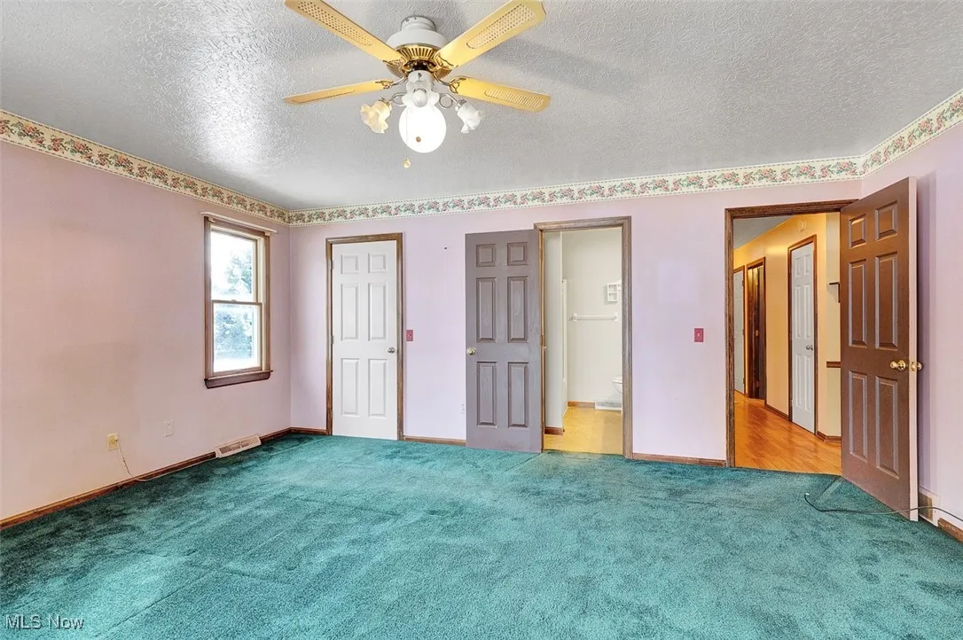 Unfurnished bedroom with a textured ceiling, carpet flooring, a ceiling fan, and multiple closets