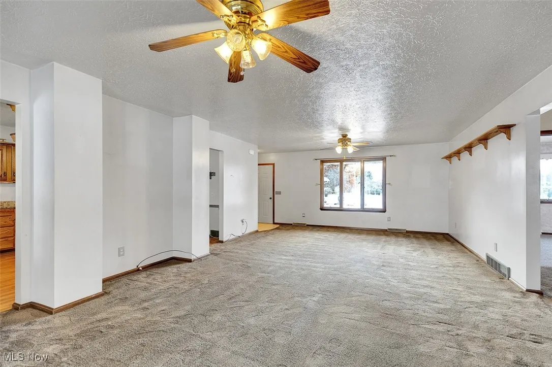 Empty room with light carpet, a ceiling fan, and a textured ceiling