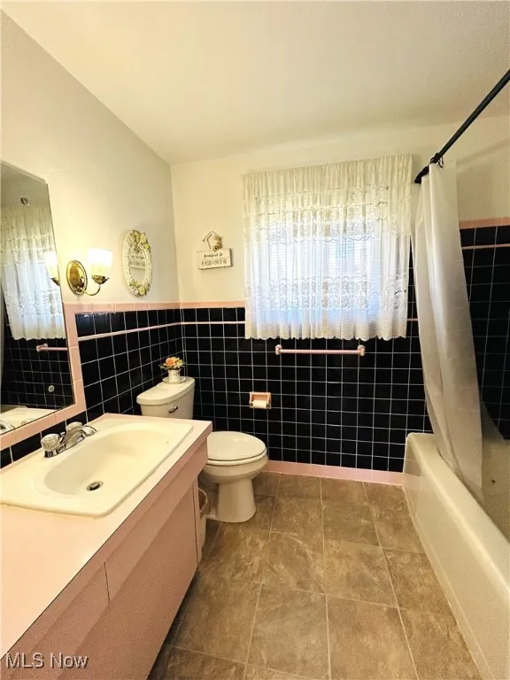 Full bathroom with shower / bath combination with curtain, vanity, tile walls, tile patterned floors, and a wainscoted wall